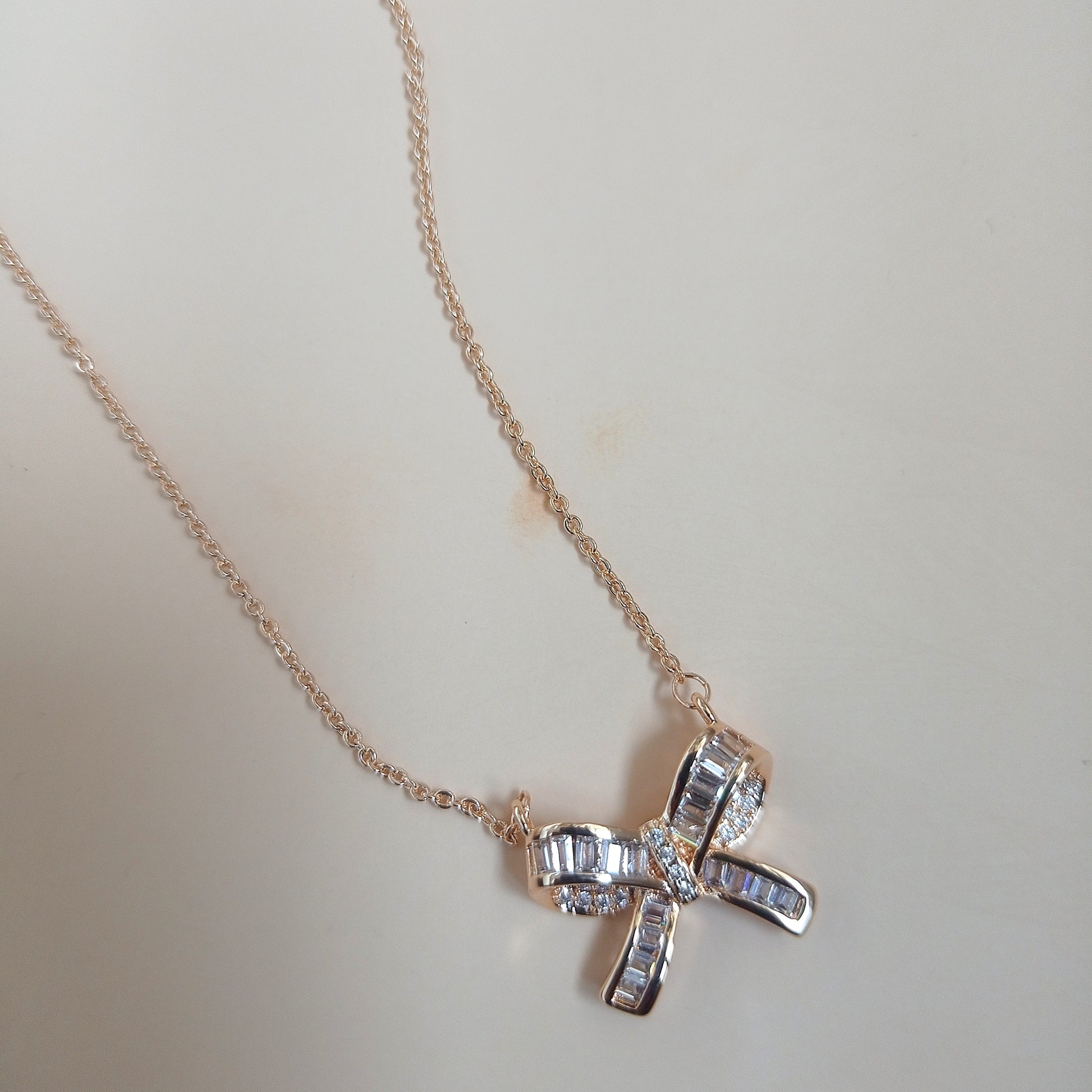 Rose gold necklace with a bow-shaped pendant featuring baguette-cut and round sparkling stones, displayed against a neutral background
