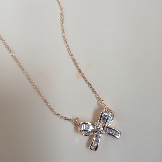 Rose gold necklace with a bow-shaped pendant featuring baguette-cut and round sparkling stones, displayed against a neutral background