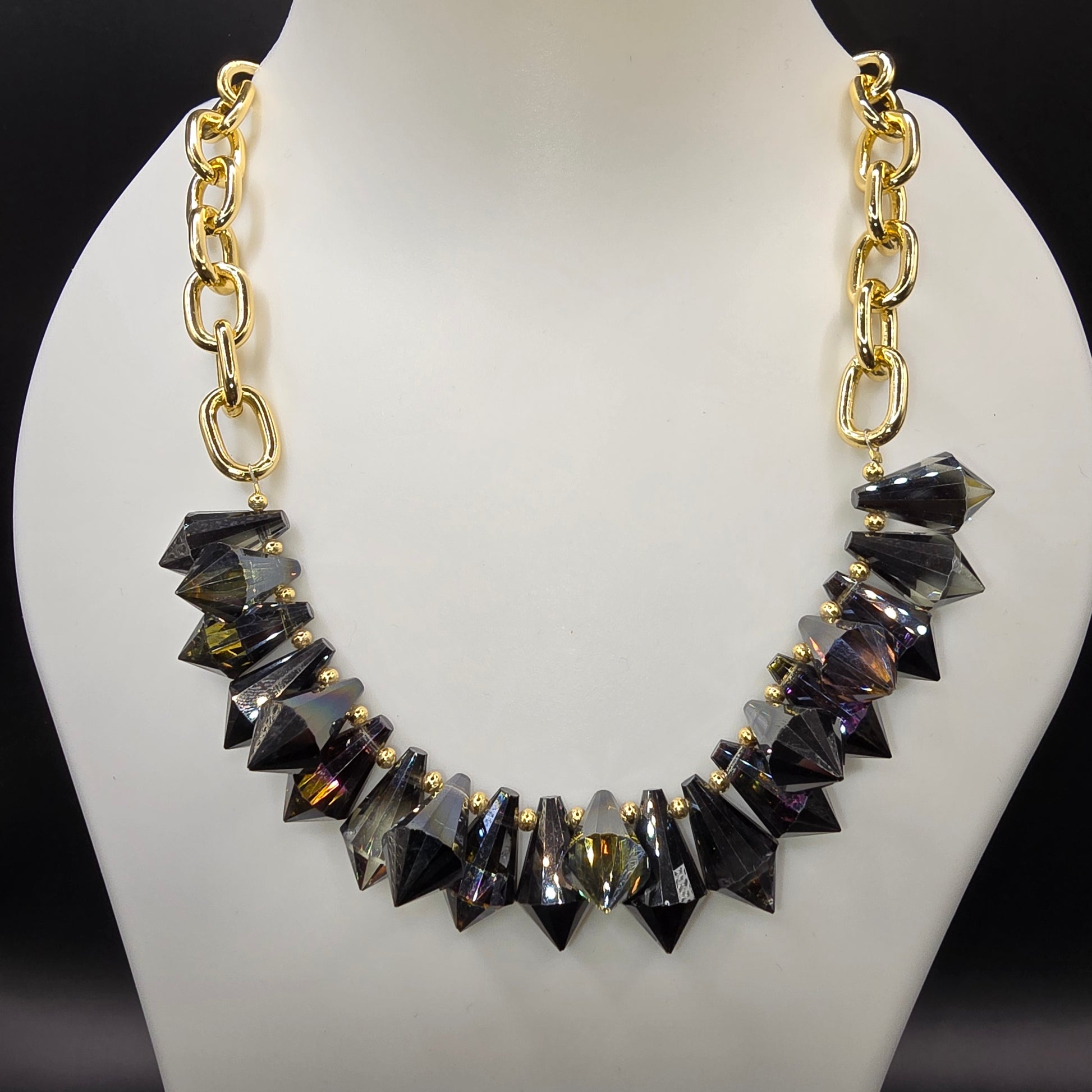 A bold and edgy statement necklace featuring faceted black crystal spikes with gold-tone accents, strung on a chunky gold chain, displayed on a mannequin bust.