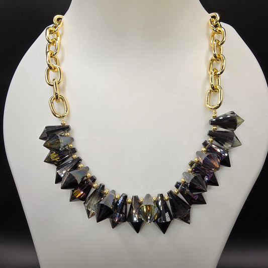 A bold and edgy statement necklace featuring faceted black crystal spikes with gold-tone accents, strung on a chunky gold chain, displayed on a mannequin bust.