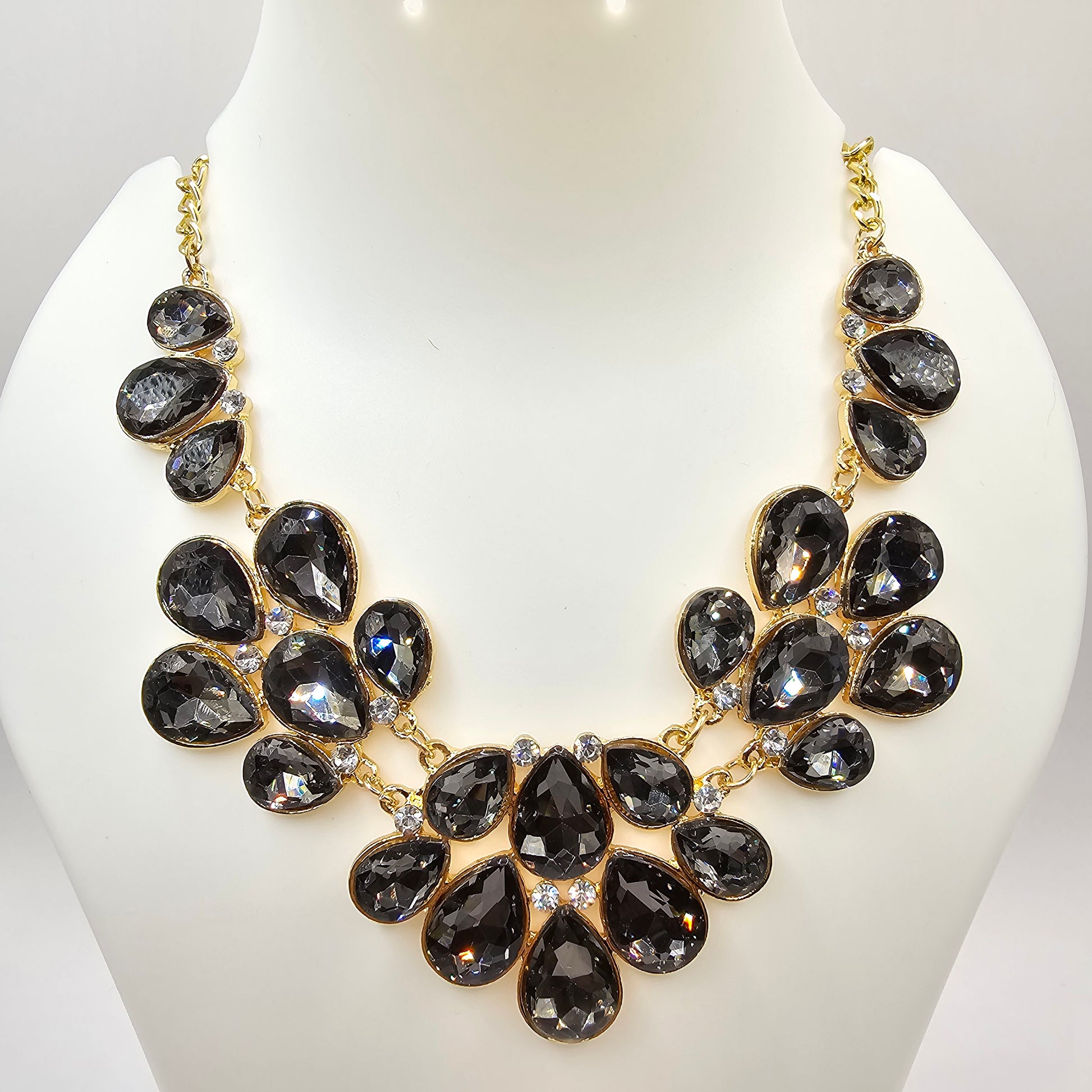 A glamorous gold-tone statement necklace adorned with faceted black teardrop crystals, elegantly arranged in a cascading floral design, displayed on a mannequin bust.