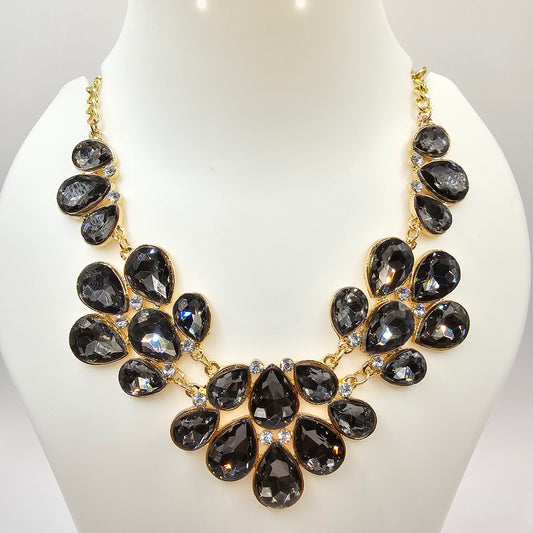 A glamorous gold-tone statement necklace adorned with faceted black teardrop crystals, elegantly arranged in a cascading floral design, displayed on a mannequin bust.