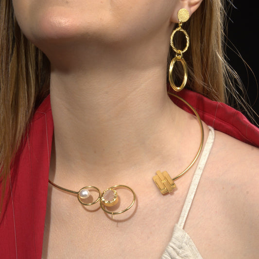  model wearing a modern open gold choker necklace featuring pearl and gemstone details, paired with statement gold dangle earrings, styled with a red blazer and neutral top
