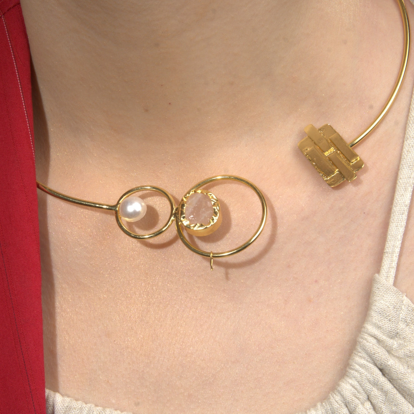  model wearing a modern open gold choker necklace featuring pearl and gemstone details, paired with statement gold dangle earrings, styled with a red blazer and neutral top