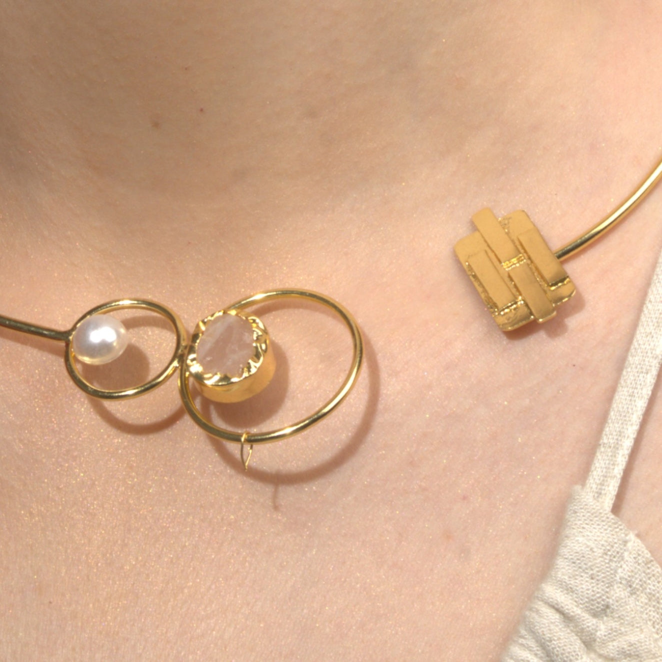  model wearing a modern open gold choker necklace featuring pearl and gemstone details, paired with statement gold dangle earrings, styled with a red blazer and neutral top