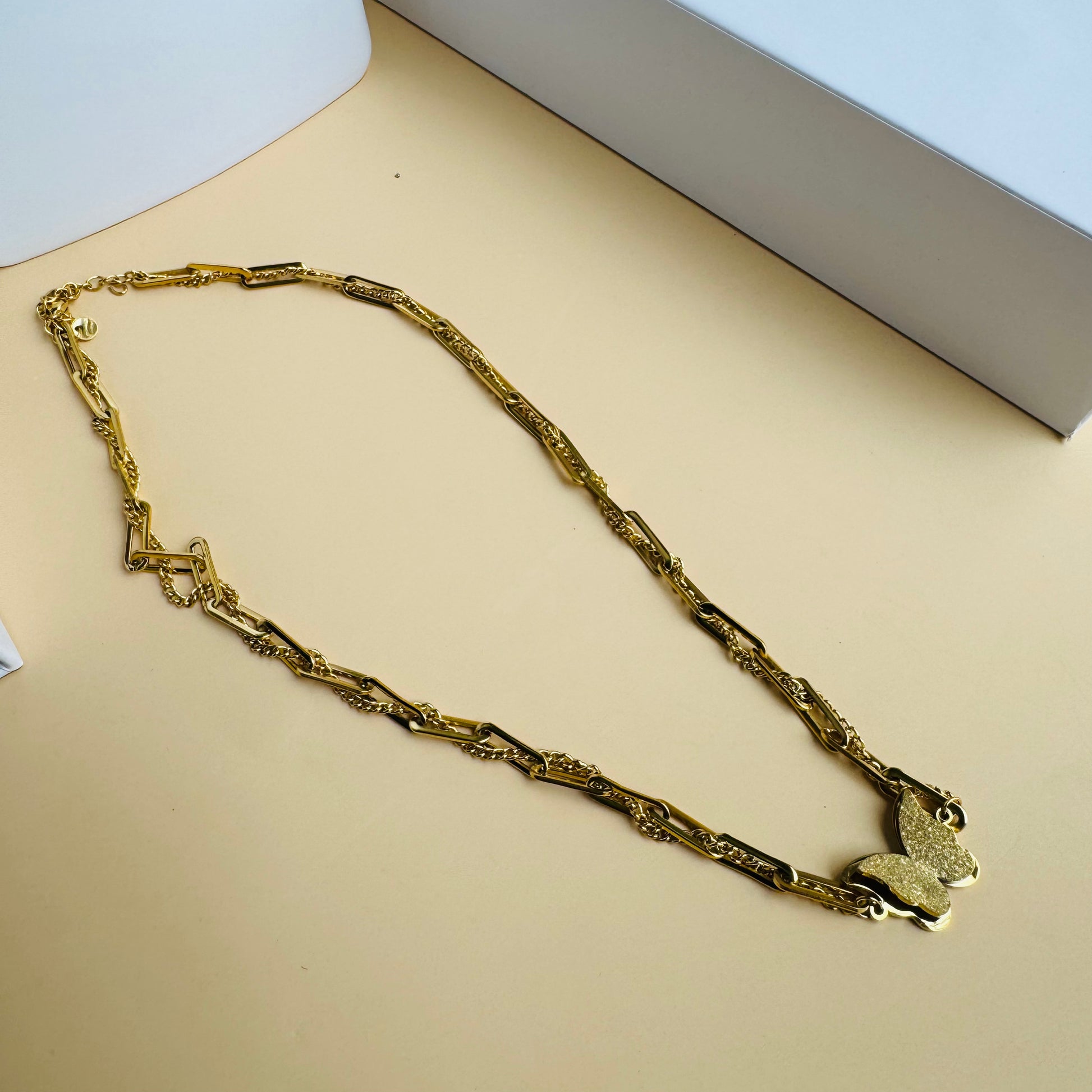 A delicate gold chain necklace featuring a butterfly pendant at its center. The chain has an intricate design, adding elegance to the minimalistic yet stylish piece. Displayed on a white mannequin bust with Lush 24 packaging in the background, creating a luxurious presentation.