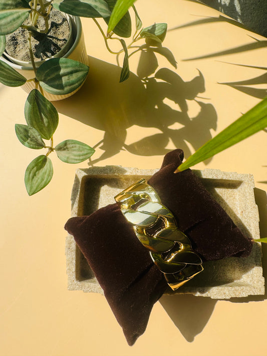 A set of gold-colored jewelry featuring the timeless link design. The set is artfully arranged on a textured tray with subtle green leaves visible in the background.