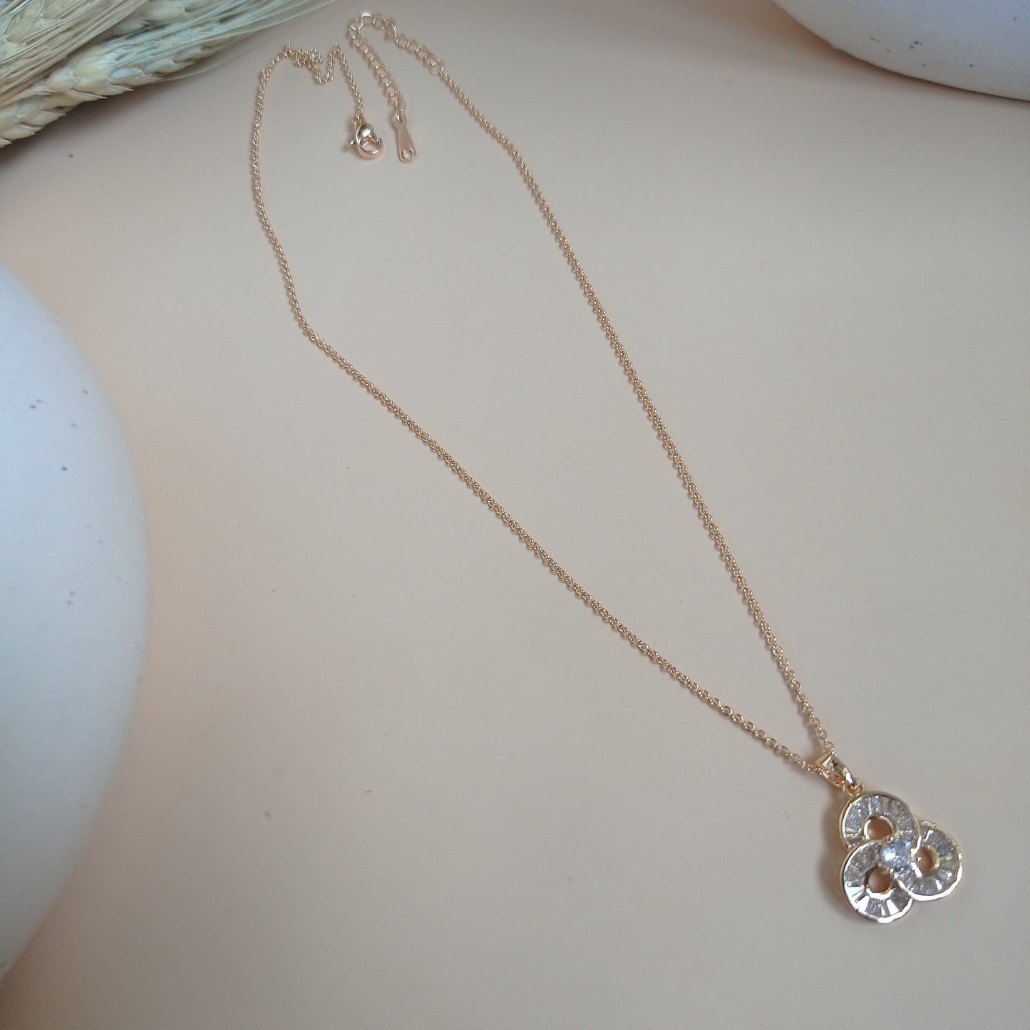 Delicate gold chain necklace with a trio-clover-shaped pendant featuring sparkling gemstones, displayed on a neutral surface