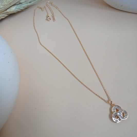 Delicate gold chain necklace with a trio-clover-shaped pendant featuring sparkling gemstones, displayed on a neutral surface