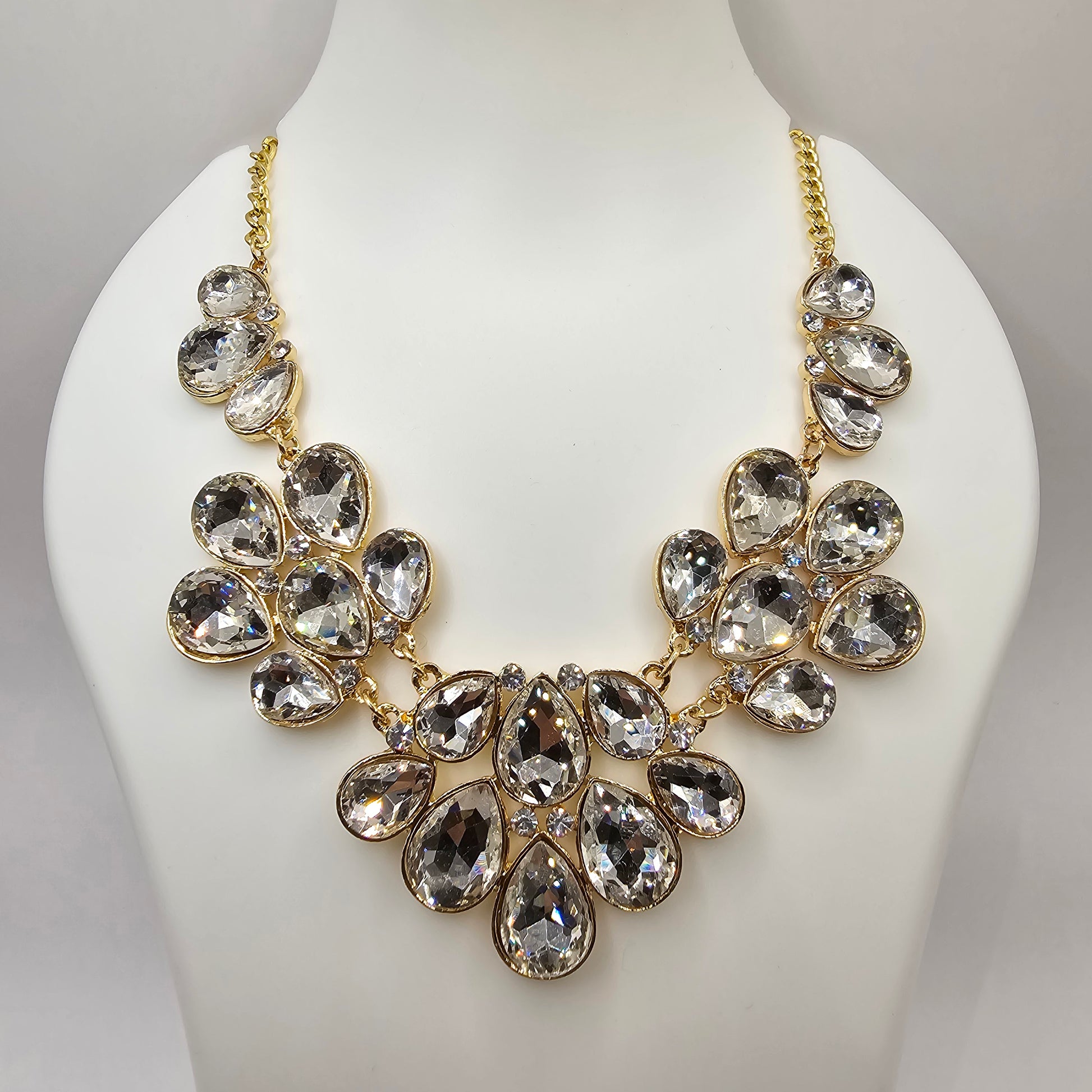 A stunning gold-tone statement necklace featuring an array of clear, faceted teardrop-shaped crystals arranged in a floral-inspired design, elegantly displayed on black satin fabric inside a jewelry box.
