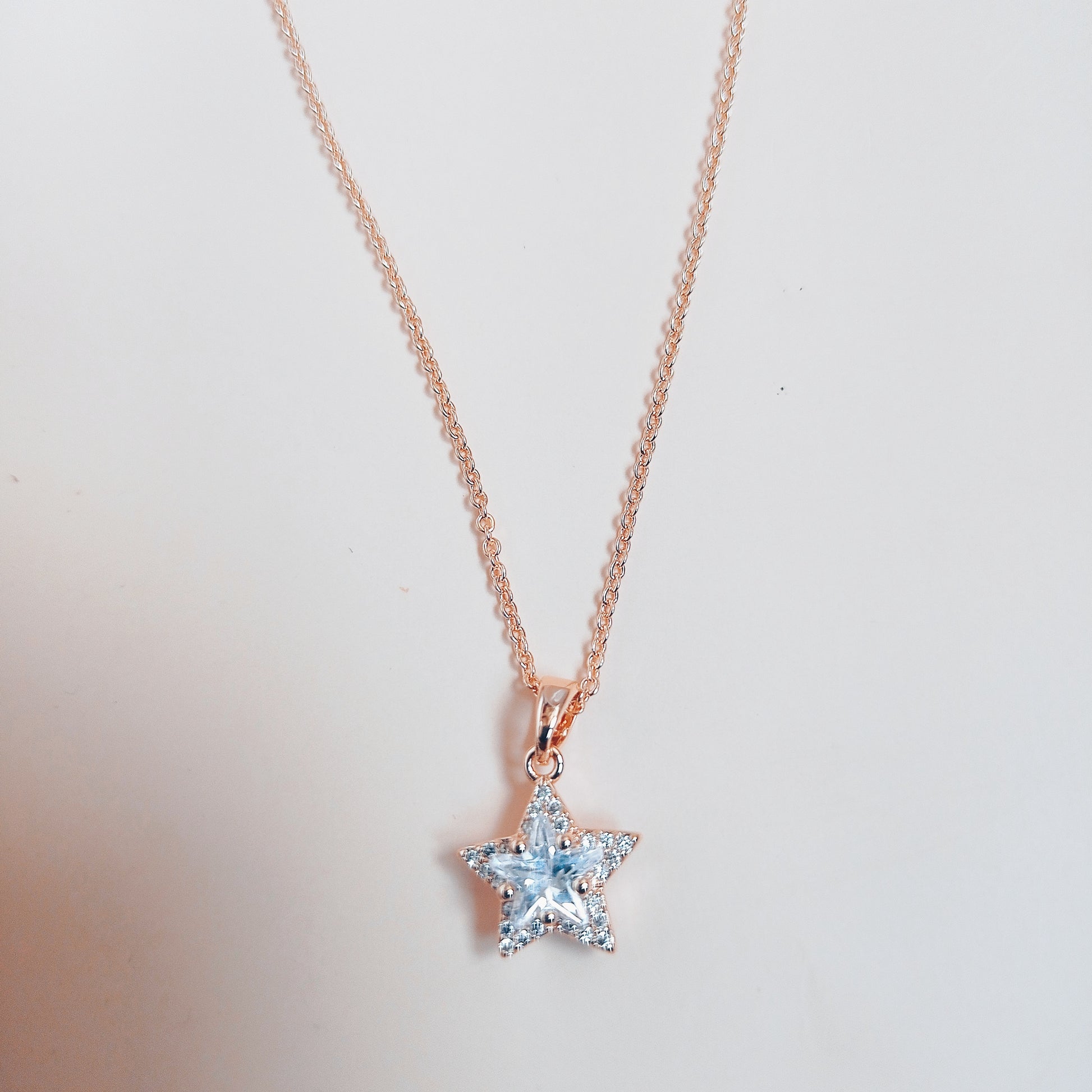 Rose gold necklace featuring a dazzling star-shaped pendant adorned with sparkling white stones, set against a soft neutral background