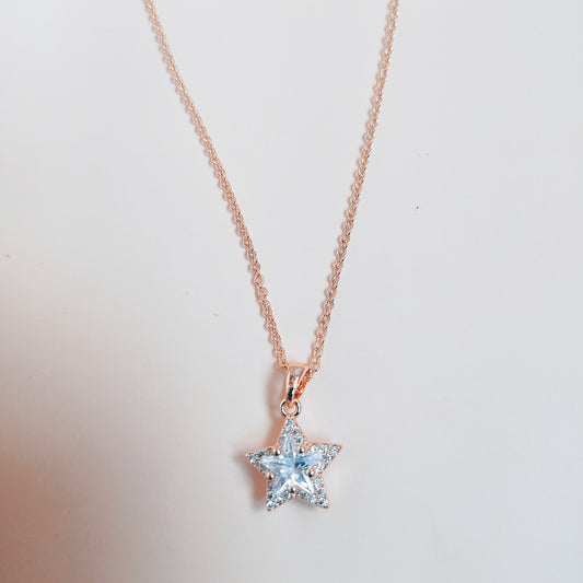 Rose gold necklace featuring a dazzling star-shaped pendant adorned with sparkling white stones, set against a soft neutral background