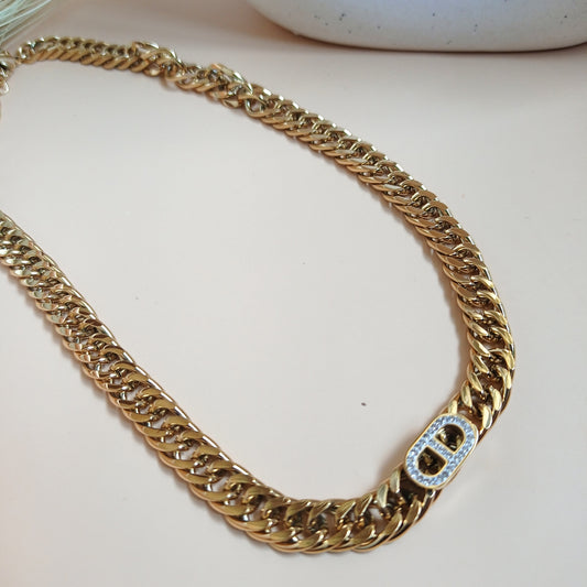 Gold-tone Cuban link chain necklace with a central embellished clasp detail, displayed on a neutral background