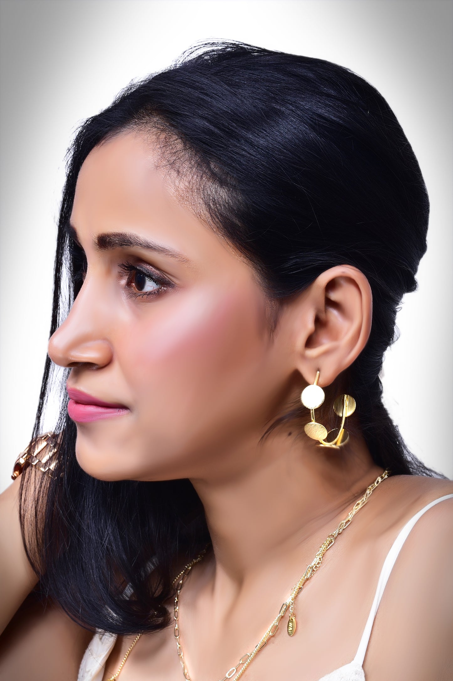 a woman wearing contemporary gold-tone statement earrings featuring multiple brushed metal discs in an artistic, asymmetric arrangement. The earrings have a modern, elegant look, perfect for adding a touch of sophistication to any outfit.
