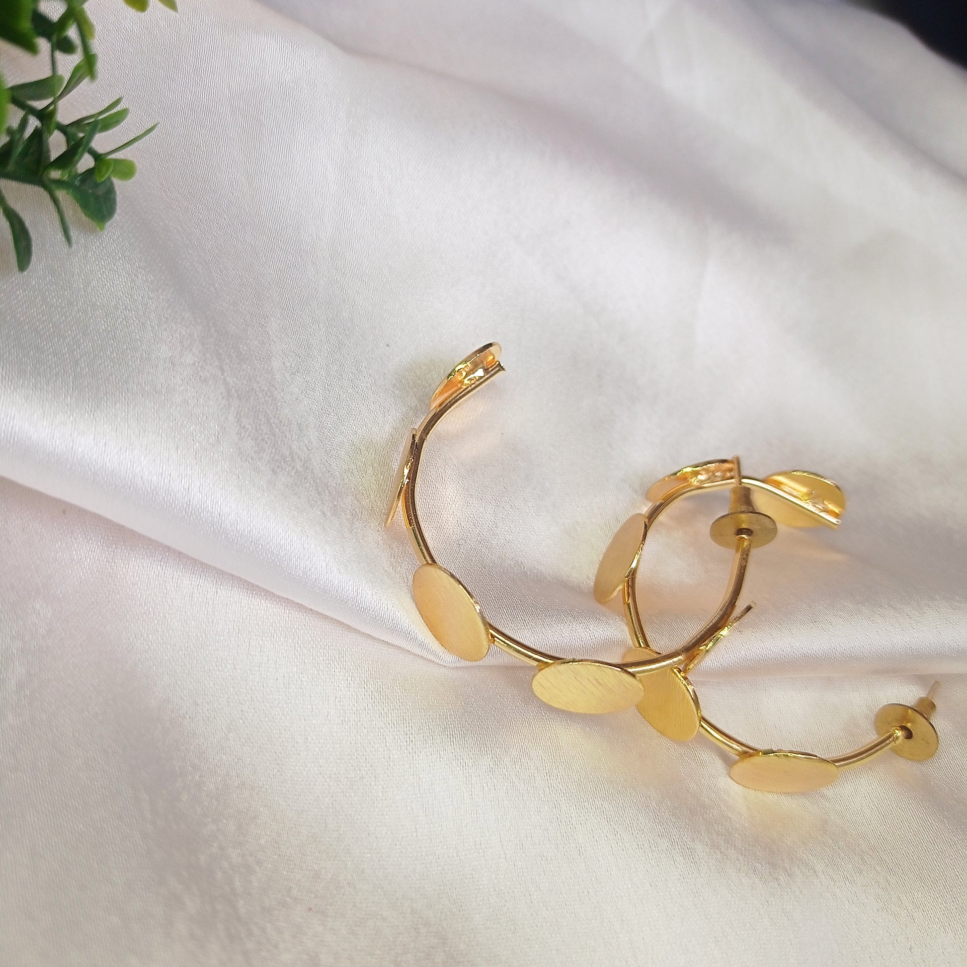 a woman wearing contemporary gold-tone statement earrings featuring multiple brushed metal discs in an artistic, asymmetric arrangement. The earrings have a modern, elegant look, perfect for adding a touch of sophistication to any outfit.