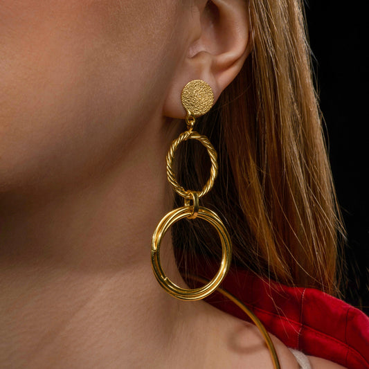 model wearing statement gold dangle earrings featuring textured and twisted circular links for a bold and modern jewelry look