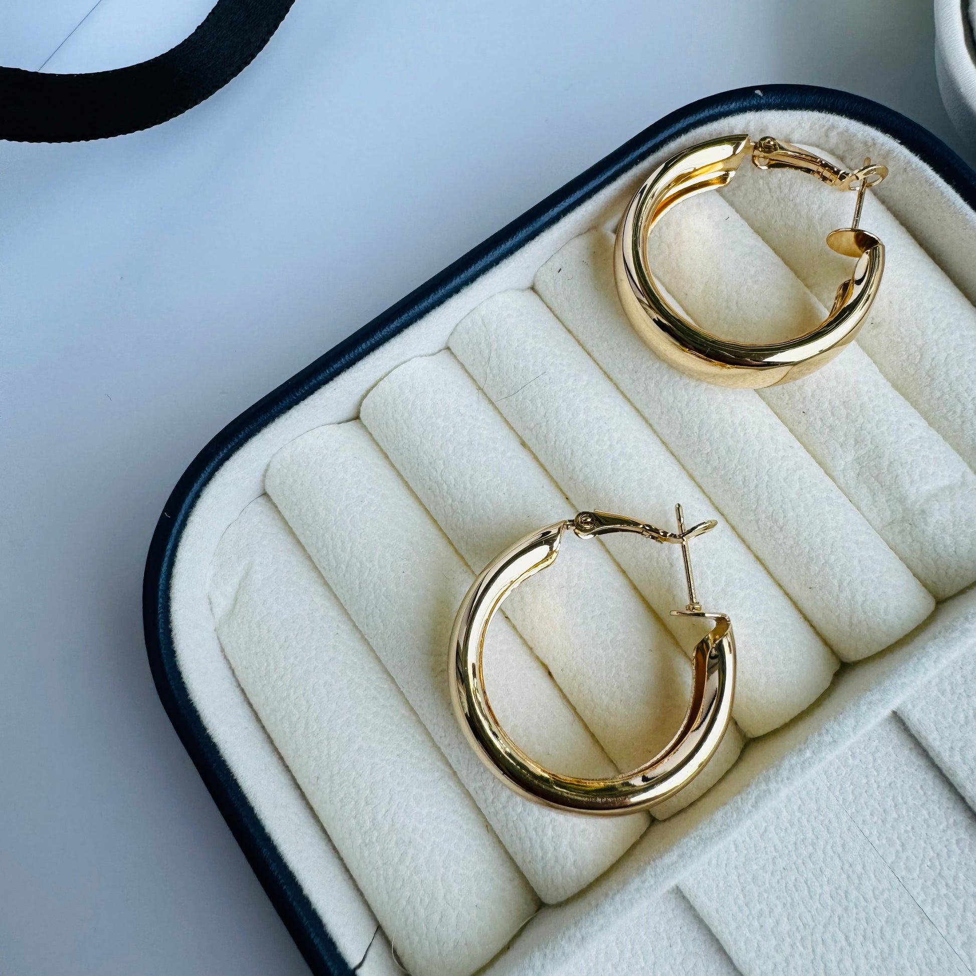 Pair of shiny gold hoop earrings in a white and black jewelry case