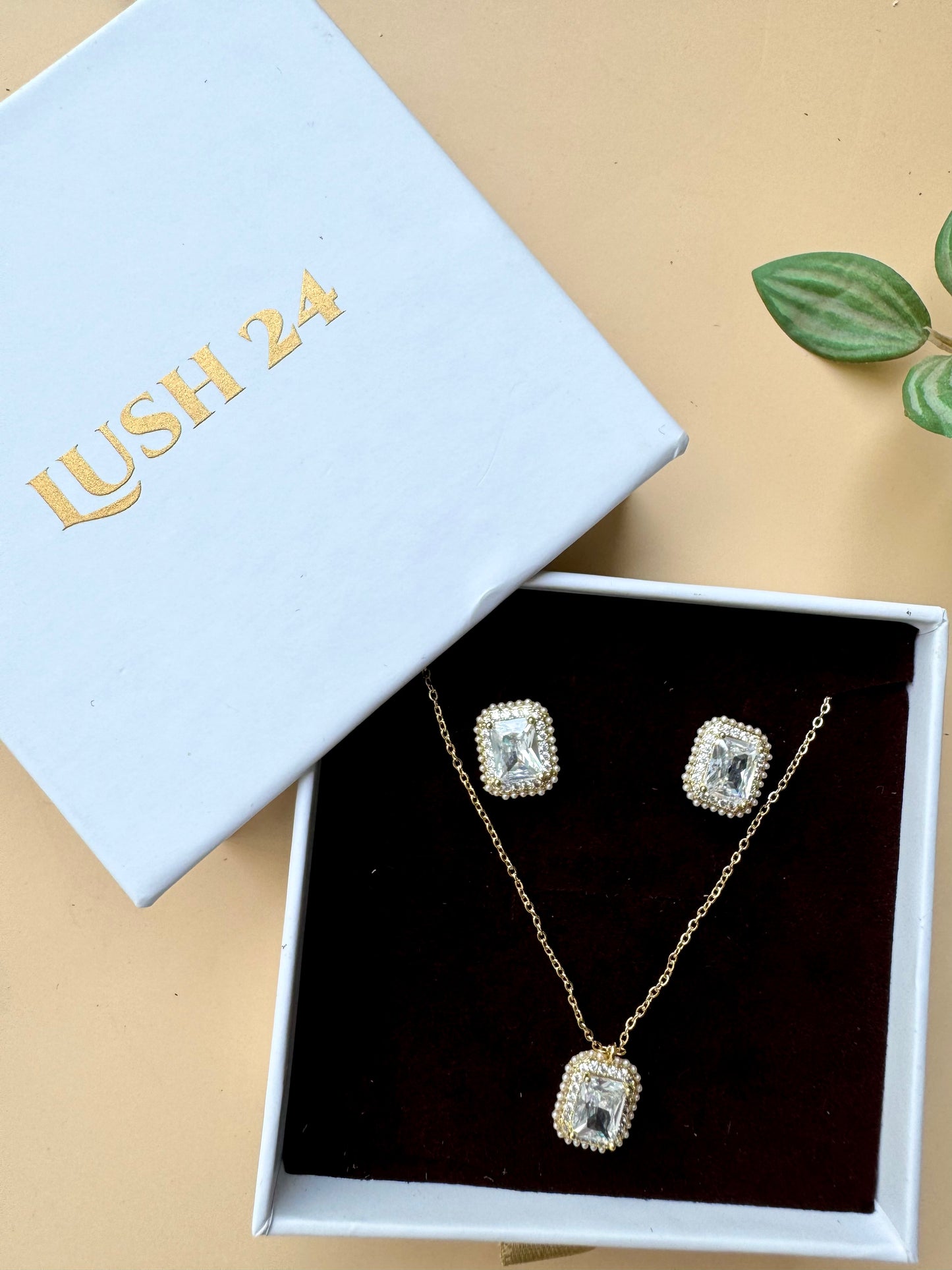 Elegant flower-shaped crystal pendant necklace and earring set displayed in a light blue and white LUSH 24 gift box.