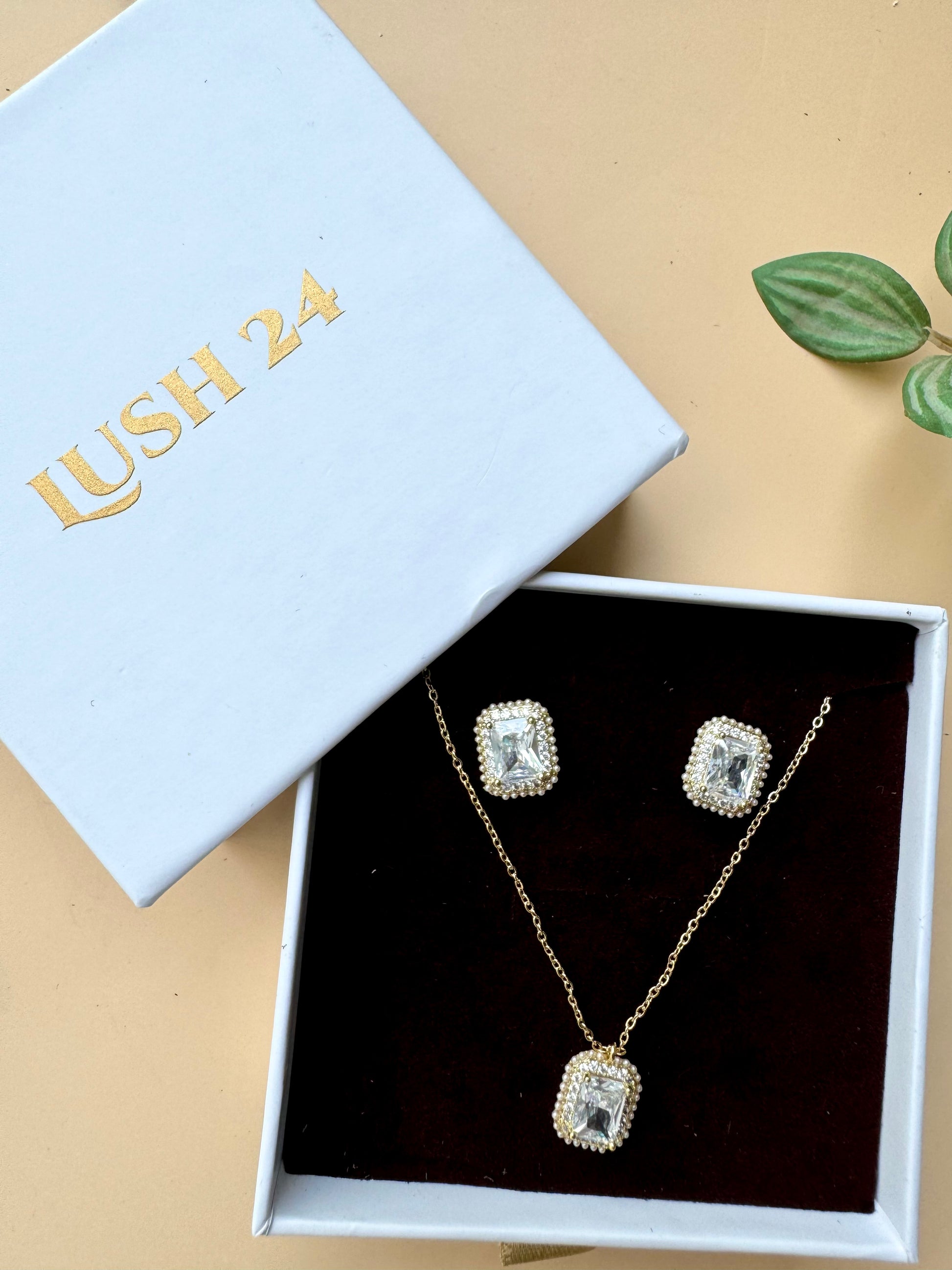 Elegant flower-shaped crystal pendant necklace and earring set displayed in a light blue and white LUSH 24 gift box.