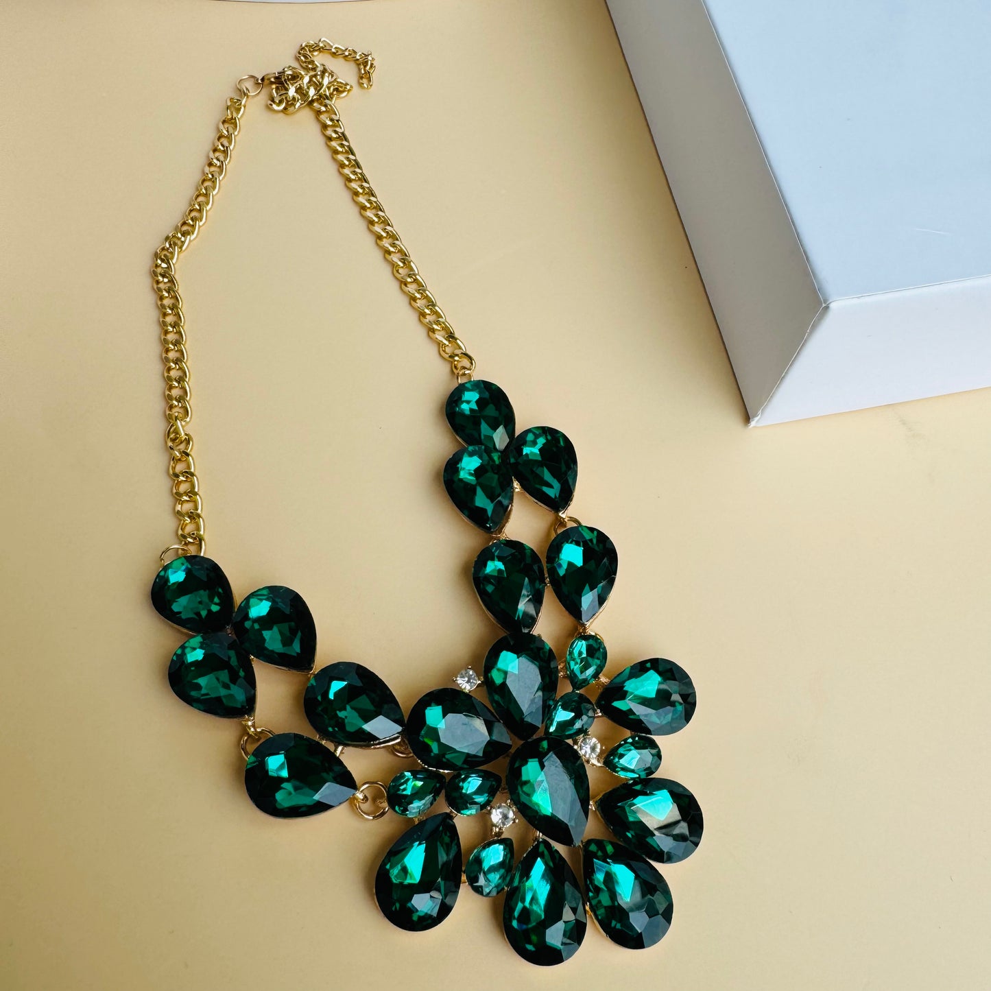 Statement necklace with faceted emerald green and black gemstones on a gold chain, displayed on a white mannequin bust. The intricate design features teardrop and oval-cut stones, creating a bold and luxurious look.