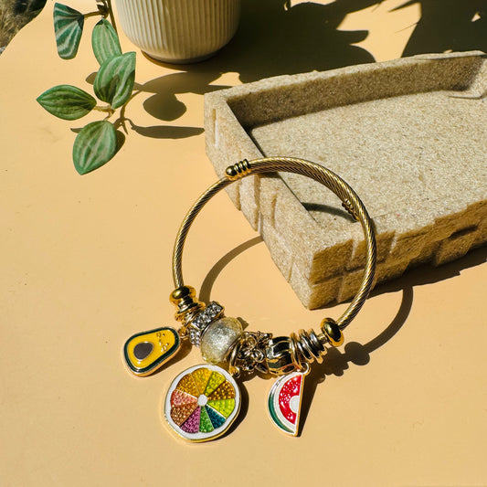 A customizable charm bracelet with a gold-toned base and several unique fruit charms. This style could be found in Mumbai.