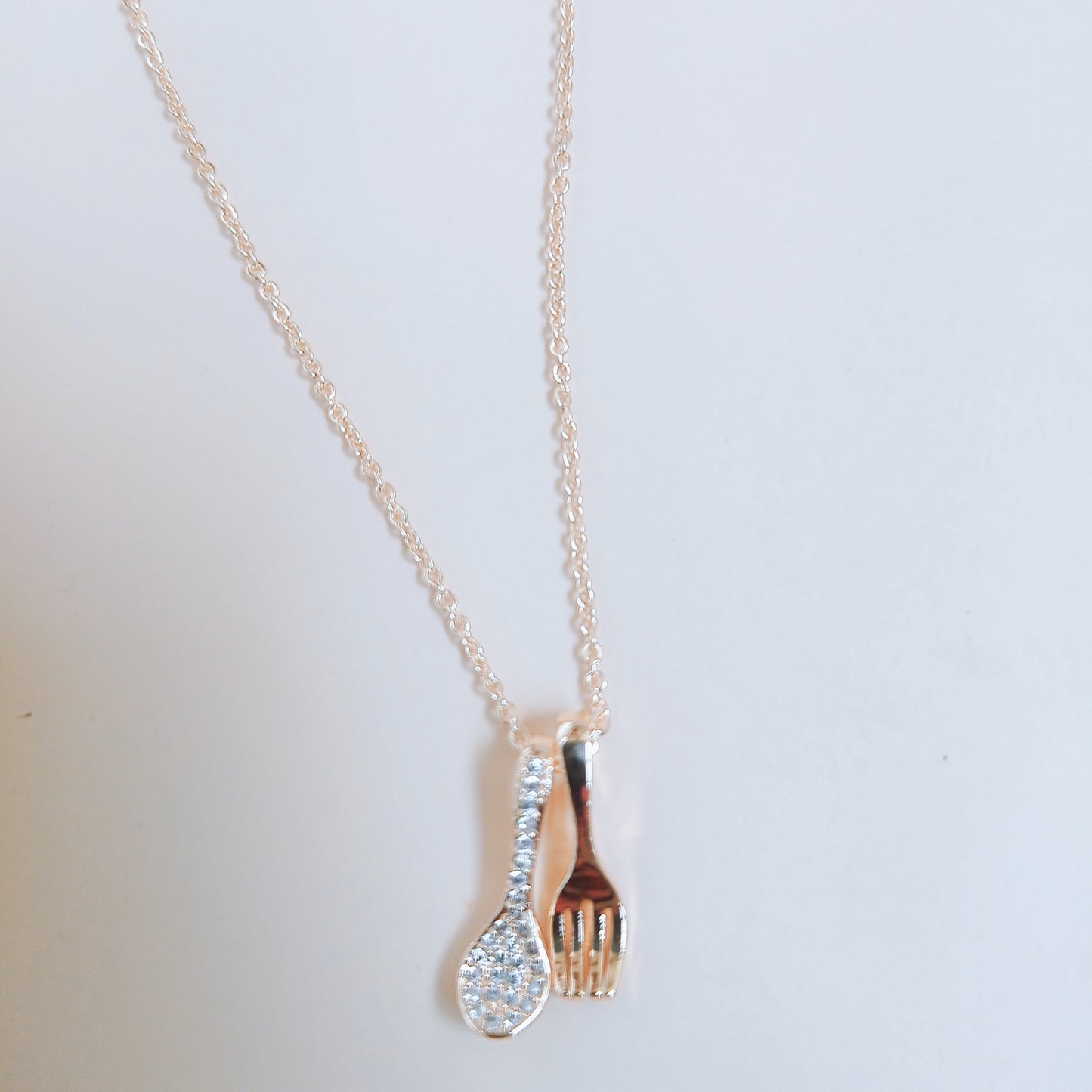 Gold chain necklace featuring a unique pendant set with a spoon adorned with sparkling gemstones and a polished fork charm, displayed on a light background