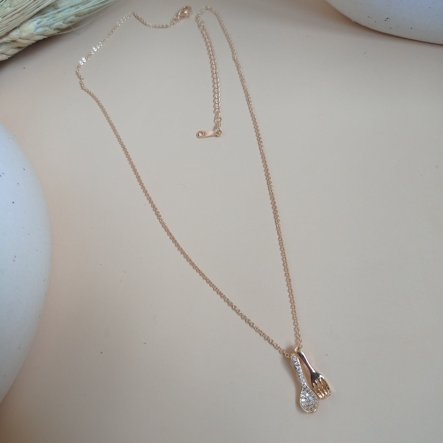 Gold chain necklace featuring a unique pendant set with a spoon adorned with sparkling gemstones and a polished fork charm, displayed on a light background
