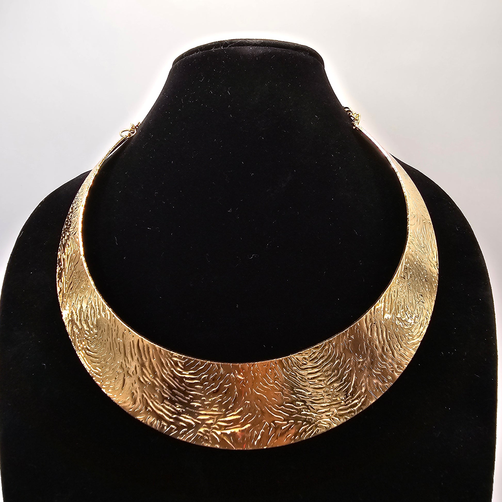 A dramatic gold metallic collar necklace with radiating spikes is displayed on a white mannequin bust. Lush 24 branded shopping bags and a jewelry box are visible in the background.