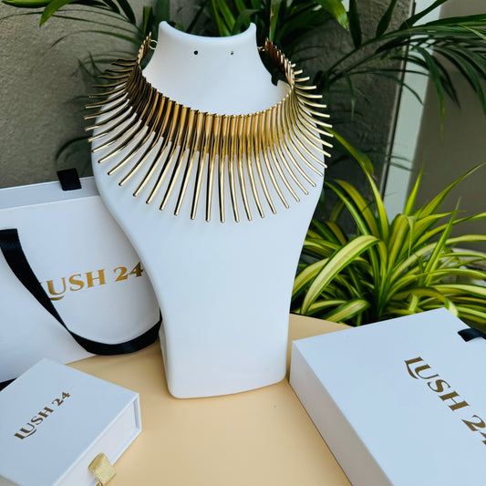 Gold statement necklace on a white display bust with Lush 24 packaging