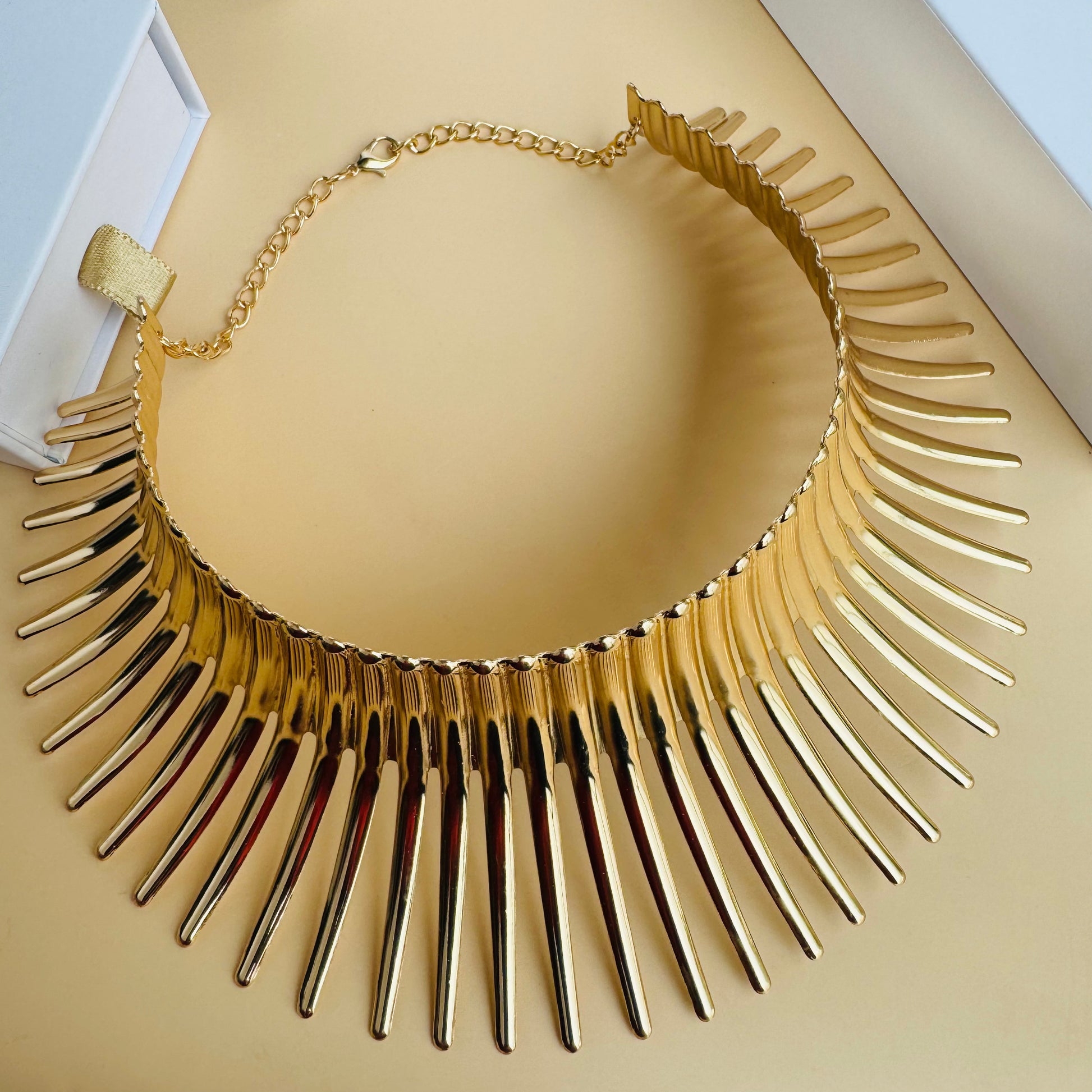 Gold statement necklace on a white display bust with Lush 24 packaging