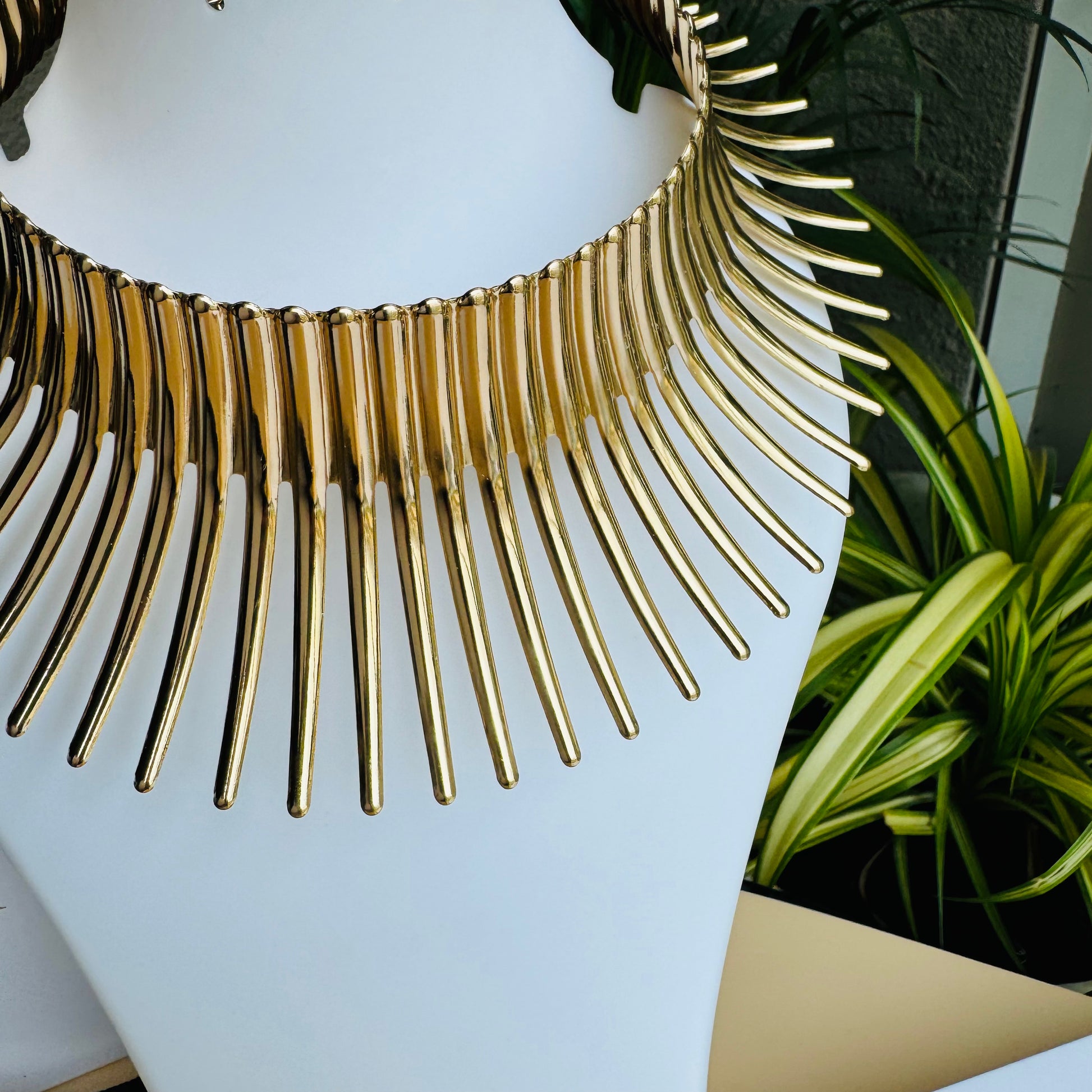 Gold statement necklace on a white display bust with Lush 24 packaging