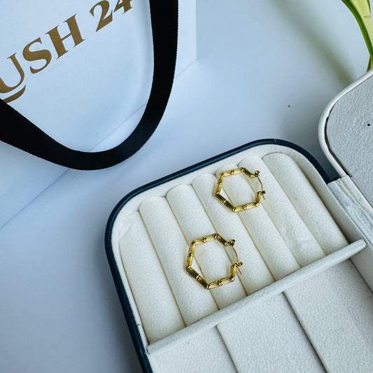 Stylish gold hexagonal hoop earrings displayed in a luxurious cream jewelry case, combining geometric elegance with modern sophistication