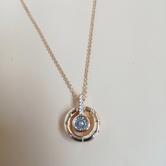 Elegant rose gold necklace with a circular pendant featuring a central blue gemstone, accented with sparkling white stones on the bail, set against a neutral background