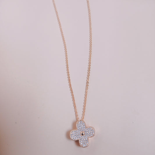 Elegant rose gold necklace with a four-leaf clover pendant encrusted with shimmering white stones, displayed against a soft pink background