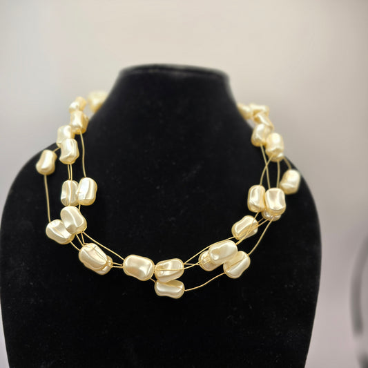 A delicate multi-strand necklace featuring irregular-shaped ivory pearls on fine gold wires, elegantly displayed on a black velvet bust.