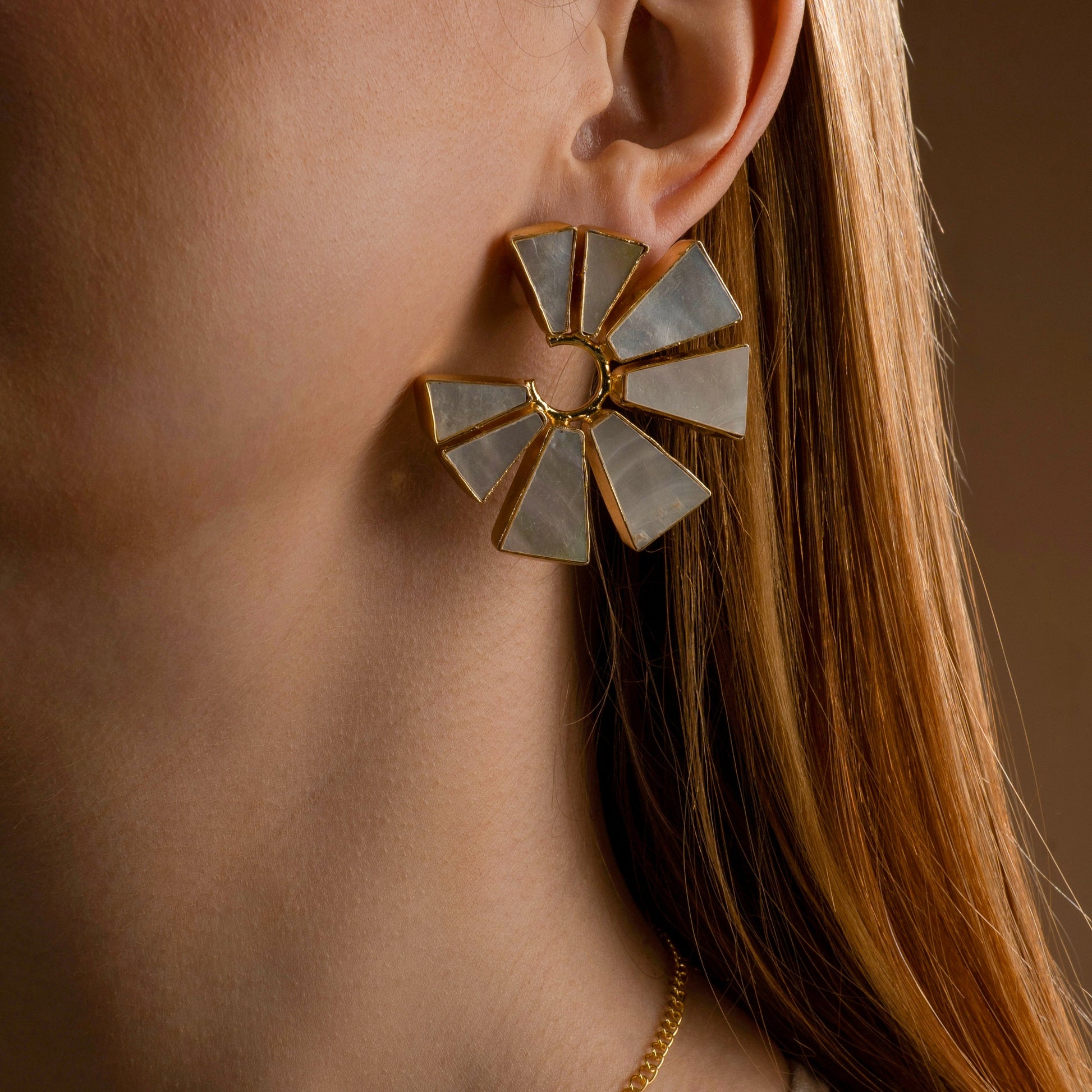 Close-up of a model wearing a statement gold and mother-of-pearl geometric fan-shaped earring, showcasing elegant and modern handcrafted jewelry
