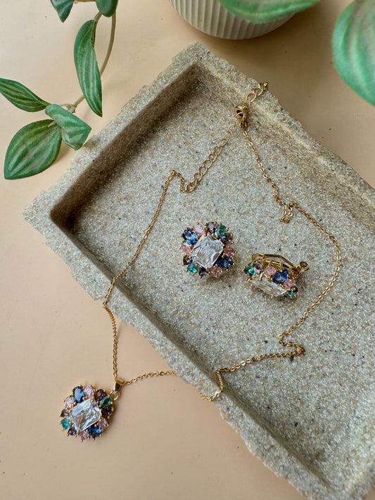 Close-up of a LUSH 24 jewelry set containing a delicate multi-toned necklace with a crystal-encrusted flower pendant and matching crystal flower stud earrings, neatly arranged in a branded box.