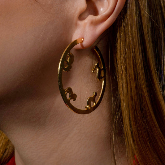 a model wearing a statement gold hoop earring with intricate cut-out detailing, highlighting bold and elegant contemporary jewelry design