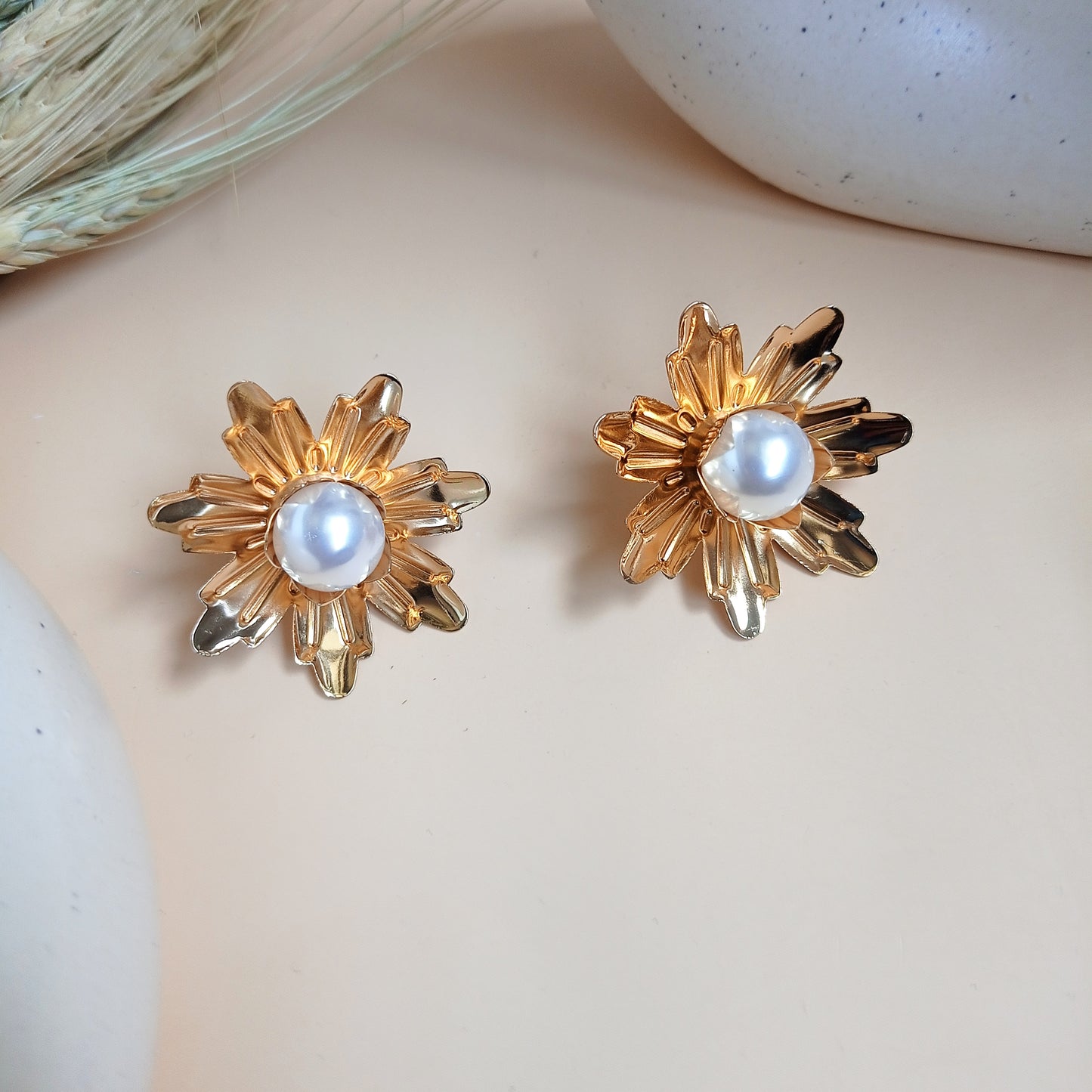 A stunning pair of gold-tone floral earrings featuring a radiant, textured petal design with a lustrous pearl at the center. These statement earrings exude vintage elegance while remaining versatile for both formal and casual looks.