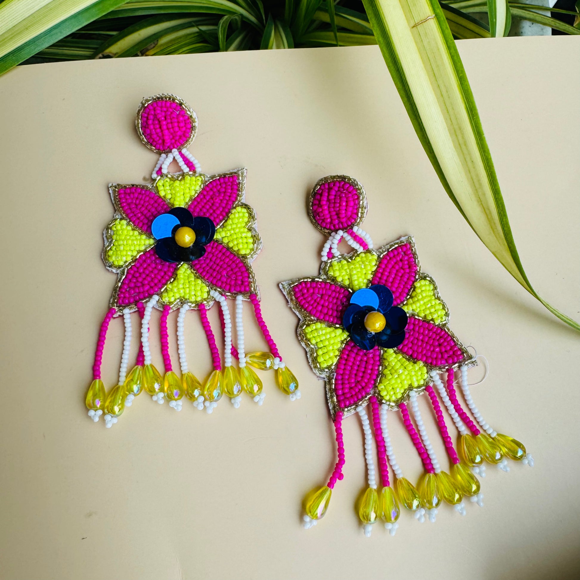Intricate beaded earrings with a central pink floral design, yellow petal-like shapes, and a beaded fringe.