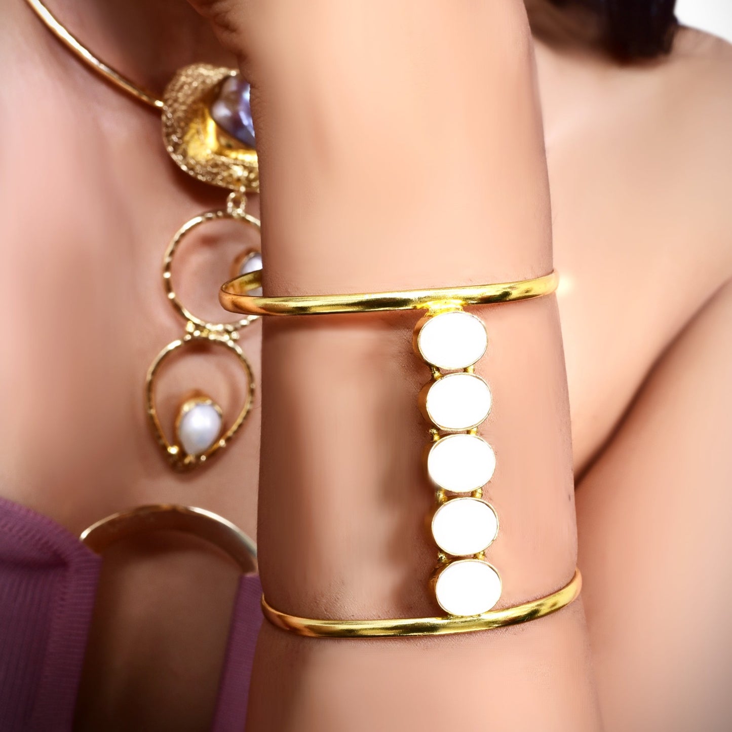 Elegant gold cuff bracelet with white circular accents, worn by a woman in a stylish mauve outfit, complementing her chic and minimalistic look.
