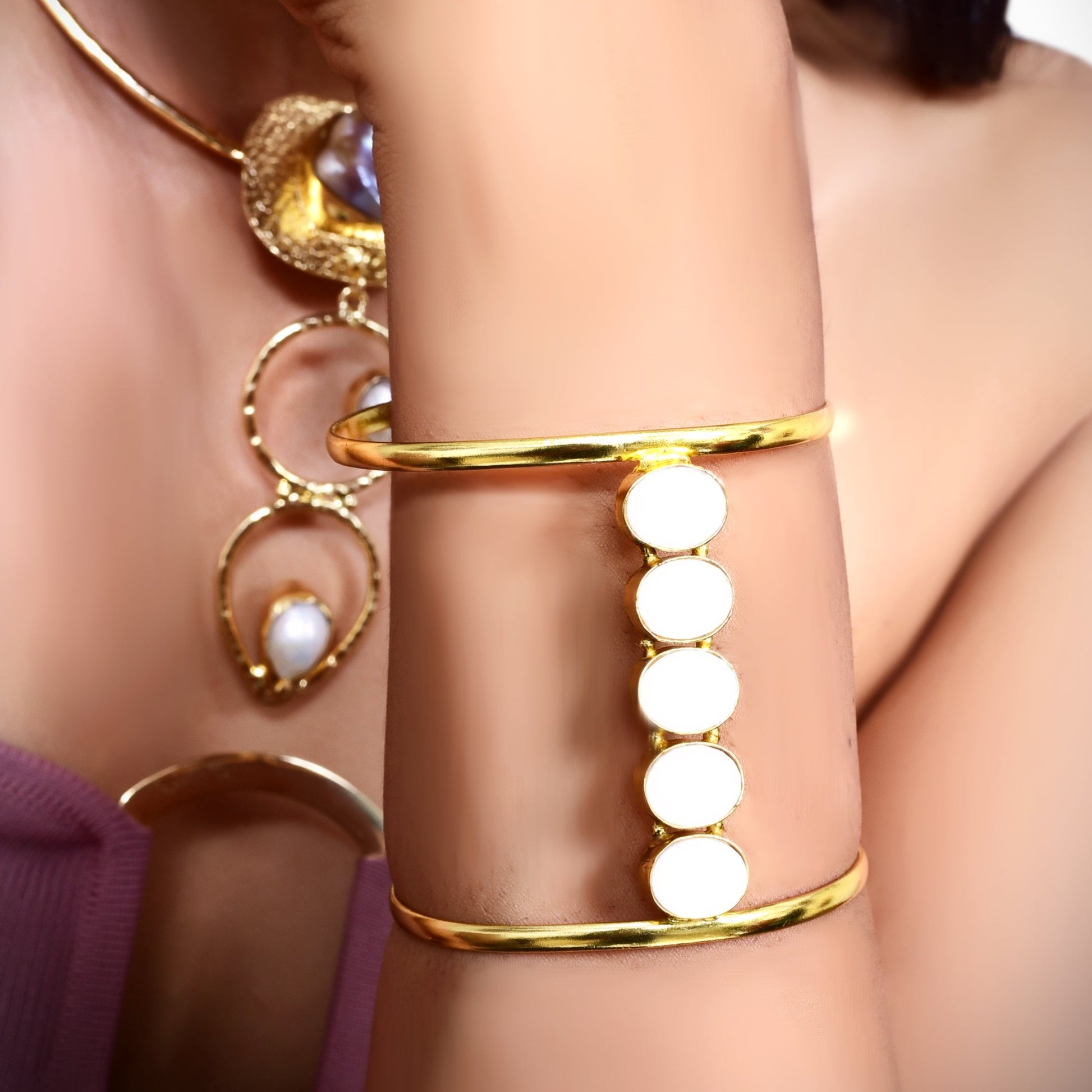Elegant gold cuff bracelet with white circular accents, worn by a woman in a stylish mauve outfit, complementing her chic and minimalistic look.
