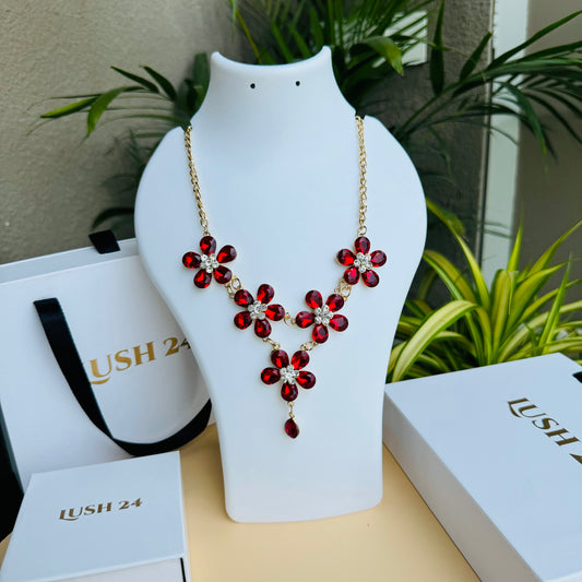 Gold statement necklace featuring red floral-shaped gemstones with a symmetrical design, displayed on a white mannequin bust. The vibrant red stones contrast beautifully with the gold chain, creating a bold and elegant look