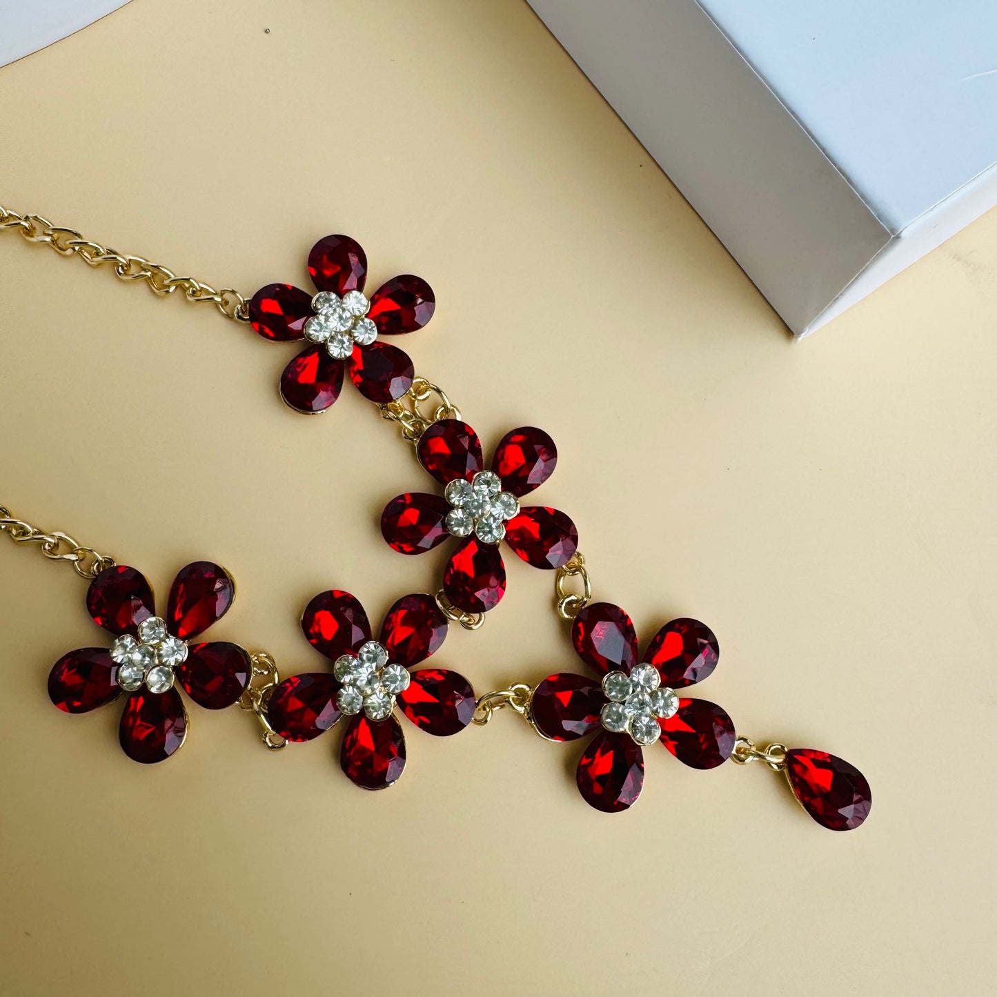 Gold statement necklace featuring red floral-shaped gemstones with a symmetrical design, displayed on a white mannequin bust. The vibrant red stones contrast beautifully with the gold chain, creating a bold and elegant look