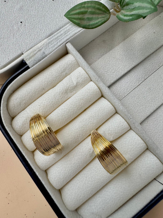 A durable and stylish gold ripple hoop earrings likely made from waterproof and tarnish-free stainless steel with an 18k gold plating, presented on a soft brown velvet pillow. 