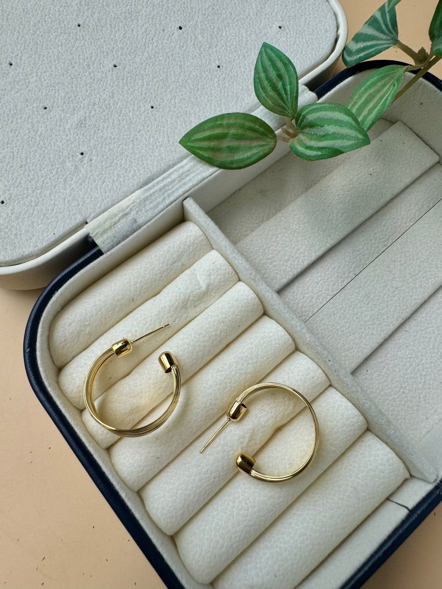 A durable and stylish gold ripple hoop earrings likely made from waterproof and tarnish-free stainless steel with an 18k gold plating, presented on a soft brown velvet pillow. 
