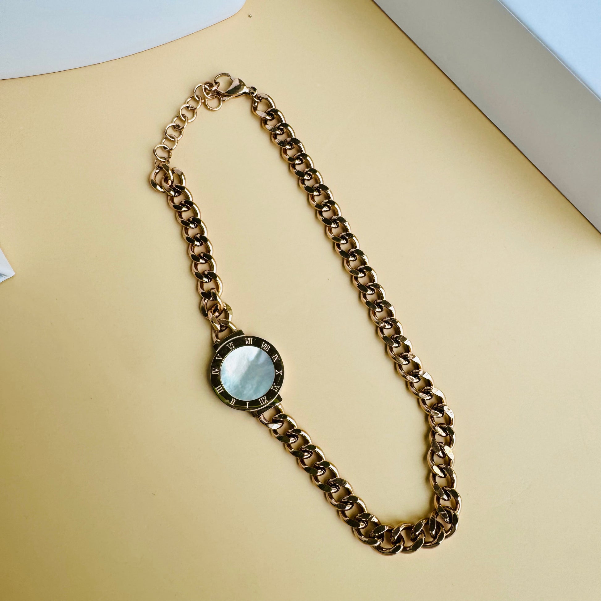 Elegant gold chain necklace with a chunky curb-link design, featuring a single circular pendant with a faceted crystal accent. The minimalist yet bold style makes it a versatile statement piece. Displayed on a white mannequin with luxury packaging in the background.