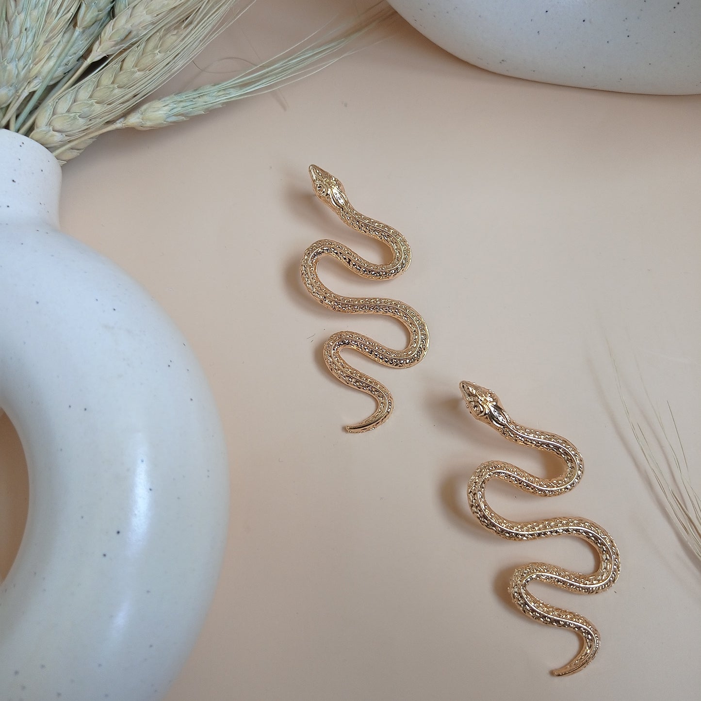 Elegant gold snake earrings with intricate detailing, draped over a modern ceramic vase, creating a bold and stylish statement accessory