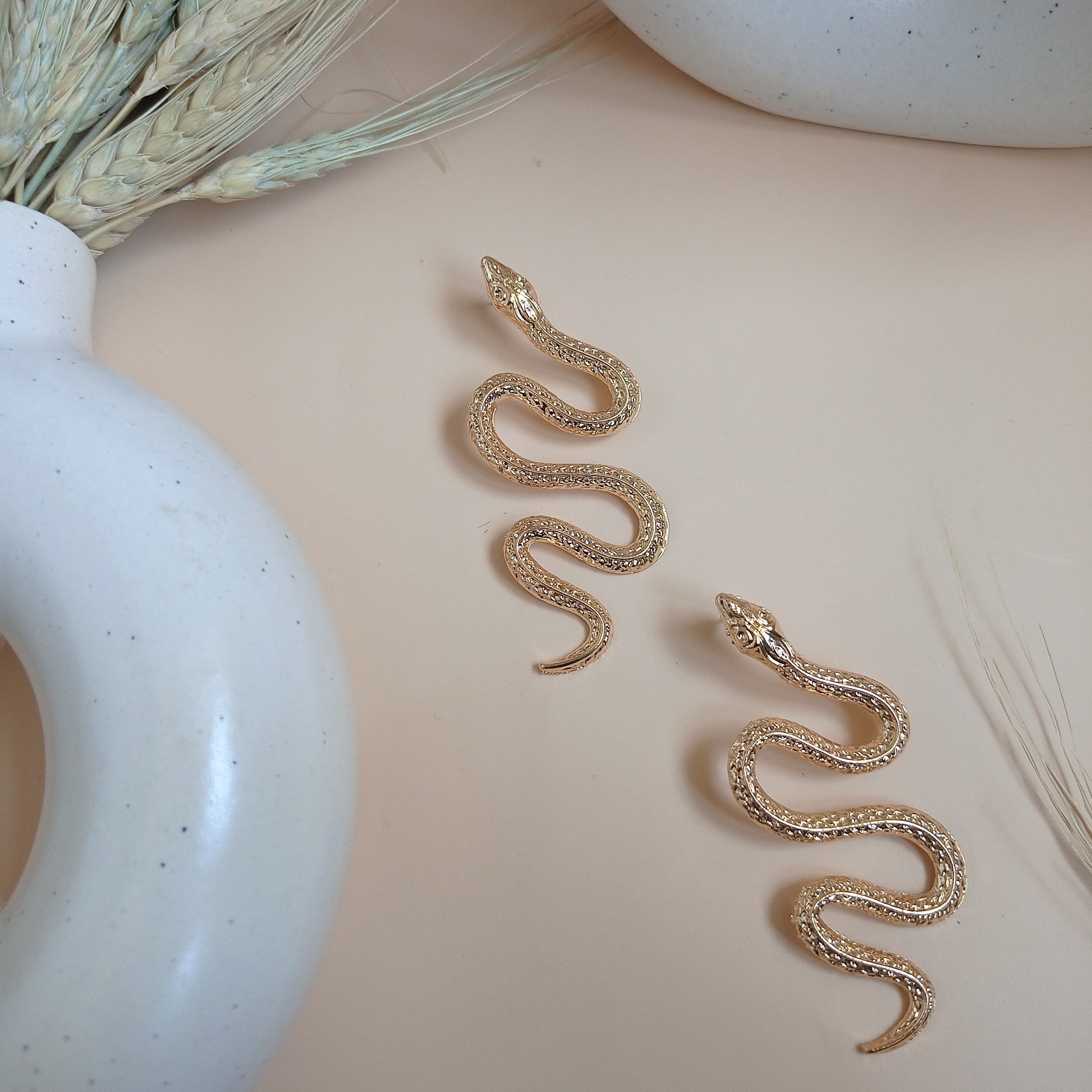Elegant gold snake earrings with intricate detailing, draped over a modern ceramic vase, creating a bold and stylish statement accessory