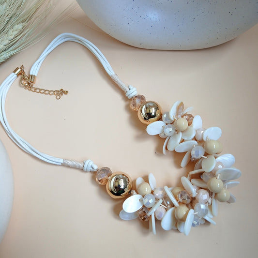 Statement necklace with white and beige floral shell beads, gold-tone accents, and a soft rope-style chain, displayed on a neutral background